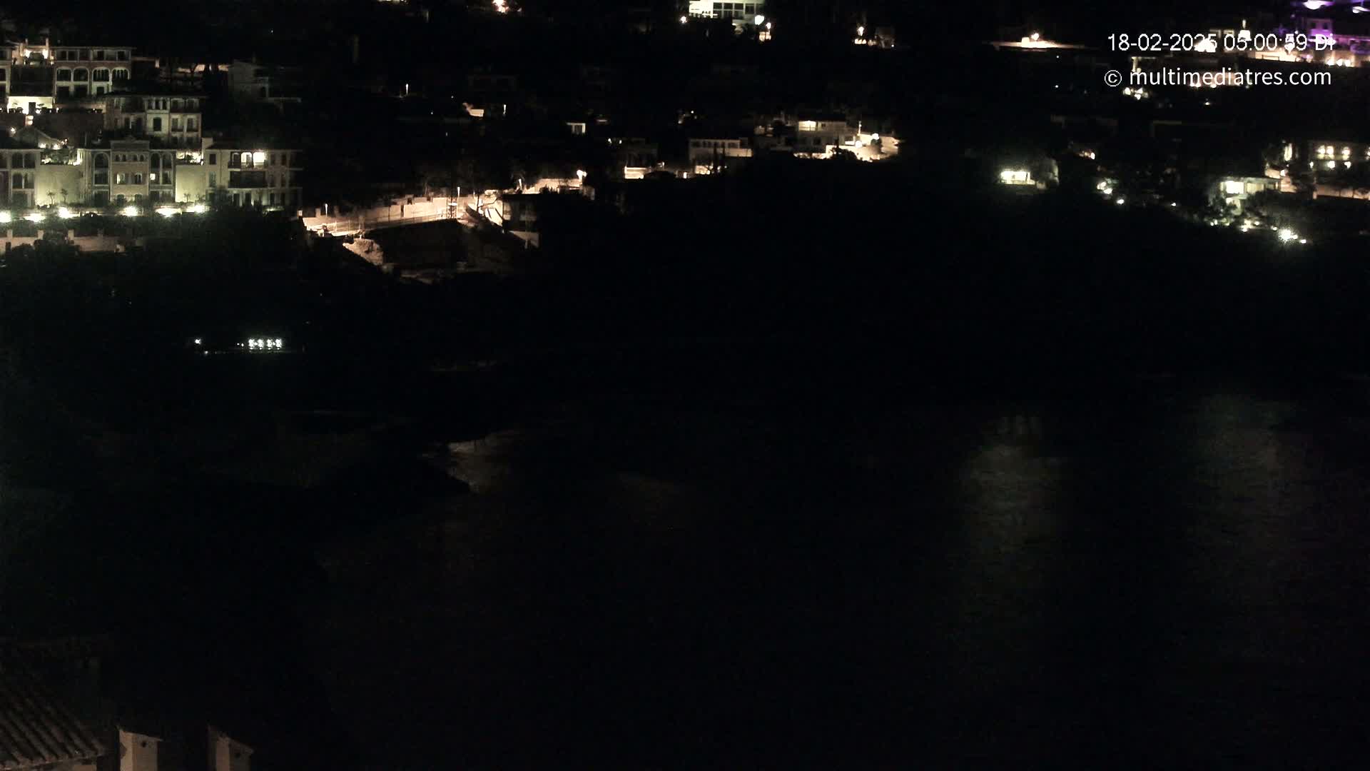 A nighttime view of a coastal town with buildings lit up and dark water below.