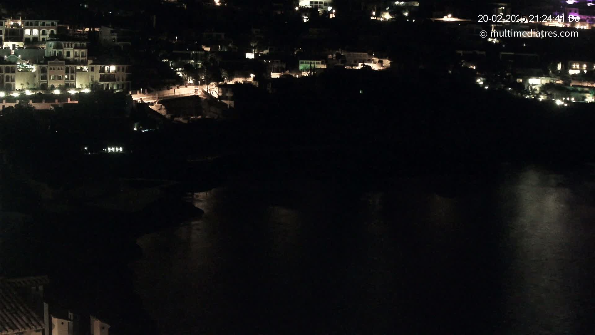 A nighttime view of a coastal town with its lights reflecting on dark water.