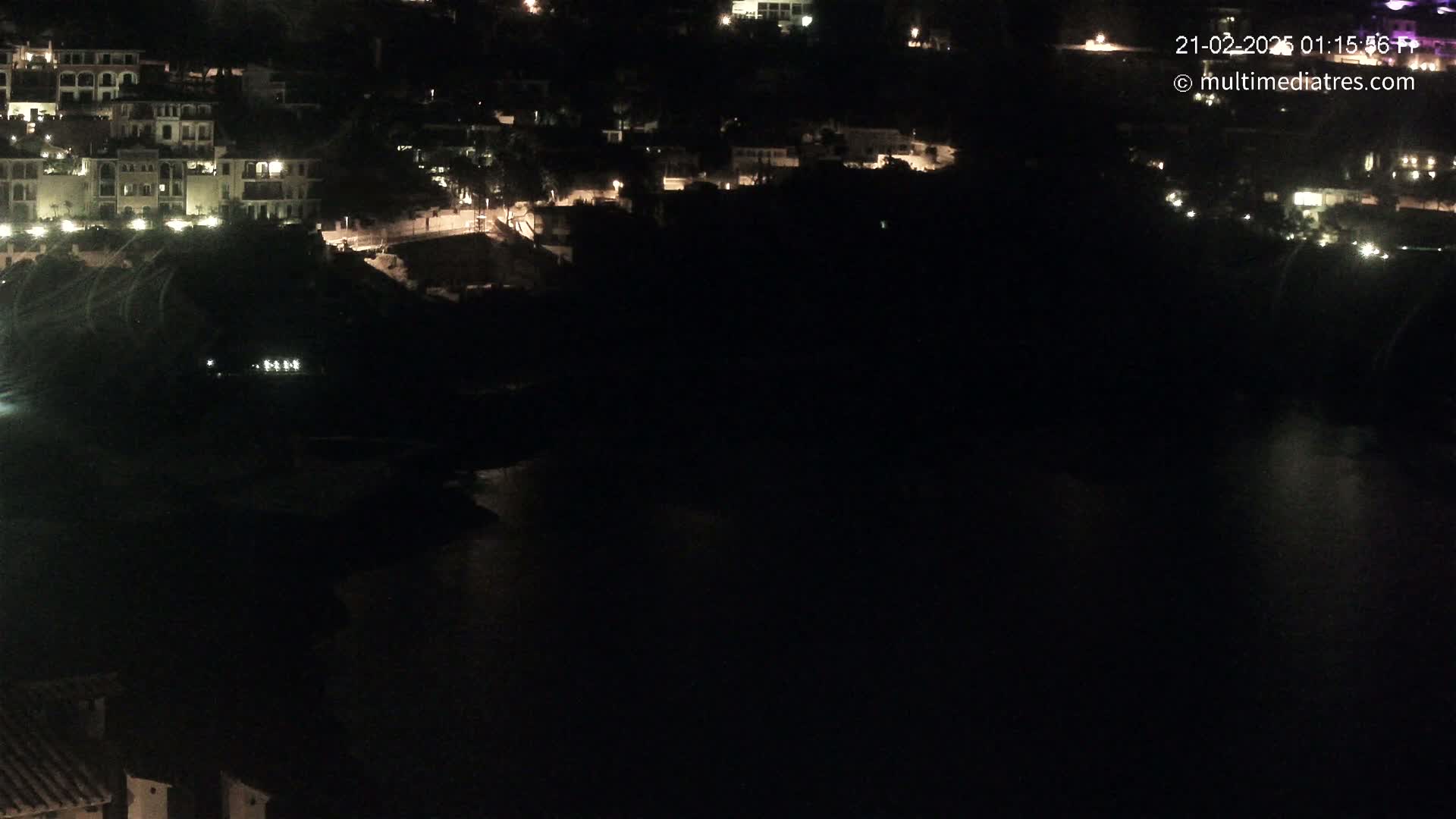 A nighttime view of a dark body of water with a hill of illuminated buildings on the opposite shore.
