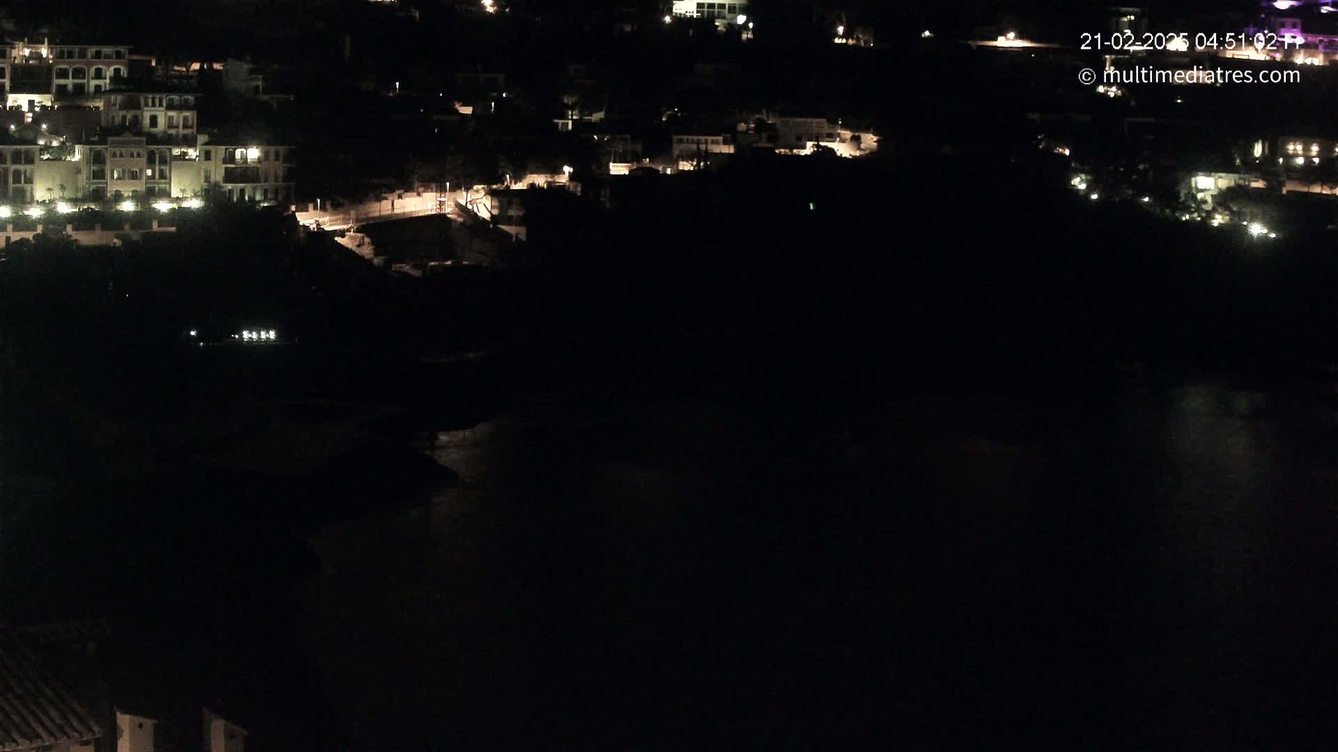 A nighttime view of a coastal town with buildings illuminated, overlooking dark water.