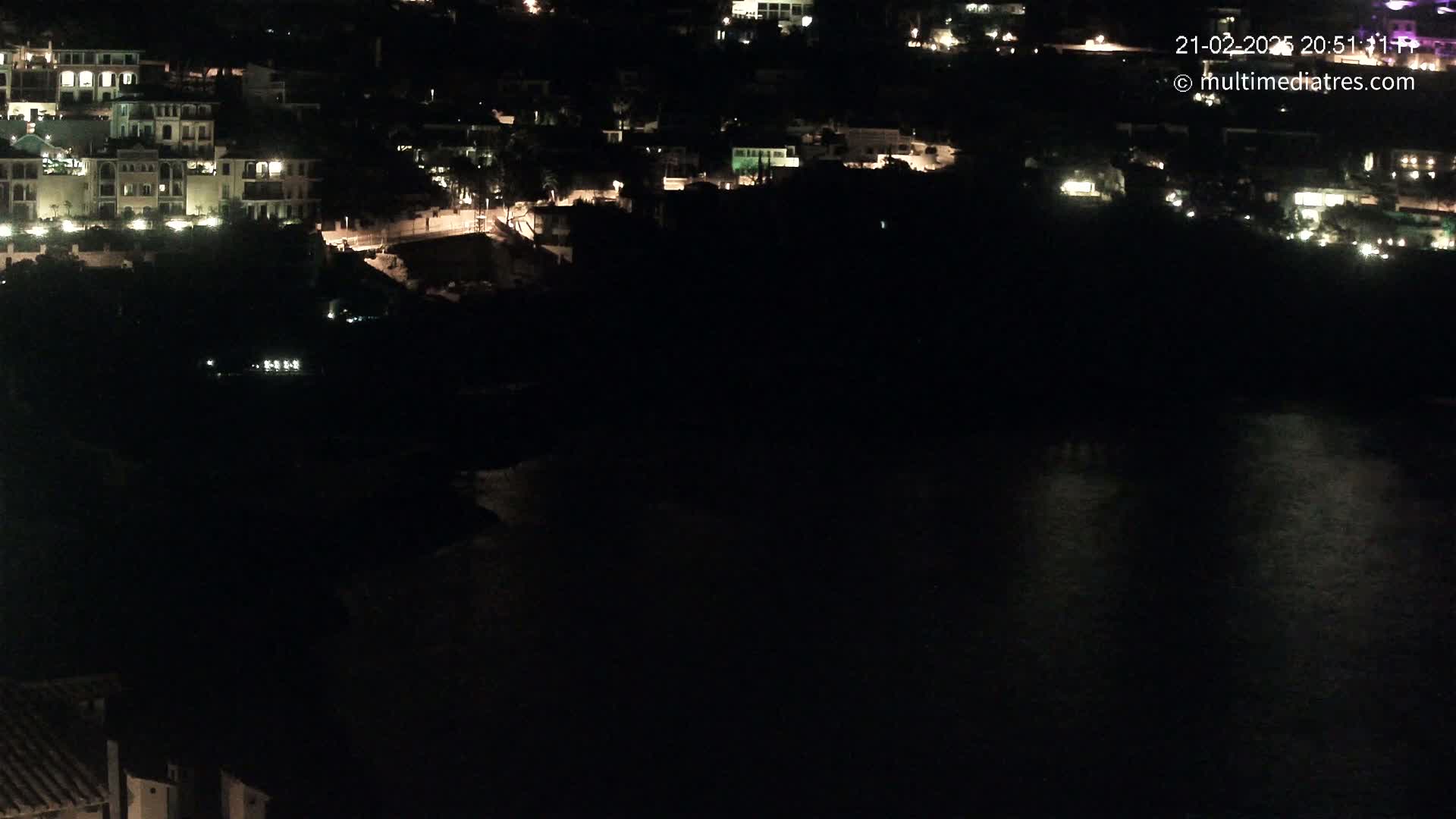 A nighttime view of a coastal town with dimly lit buildings and a dark body of water.