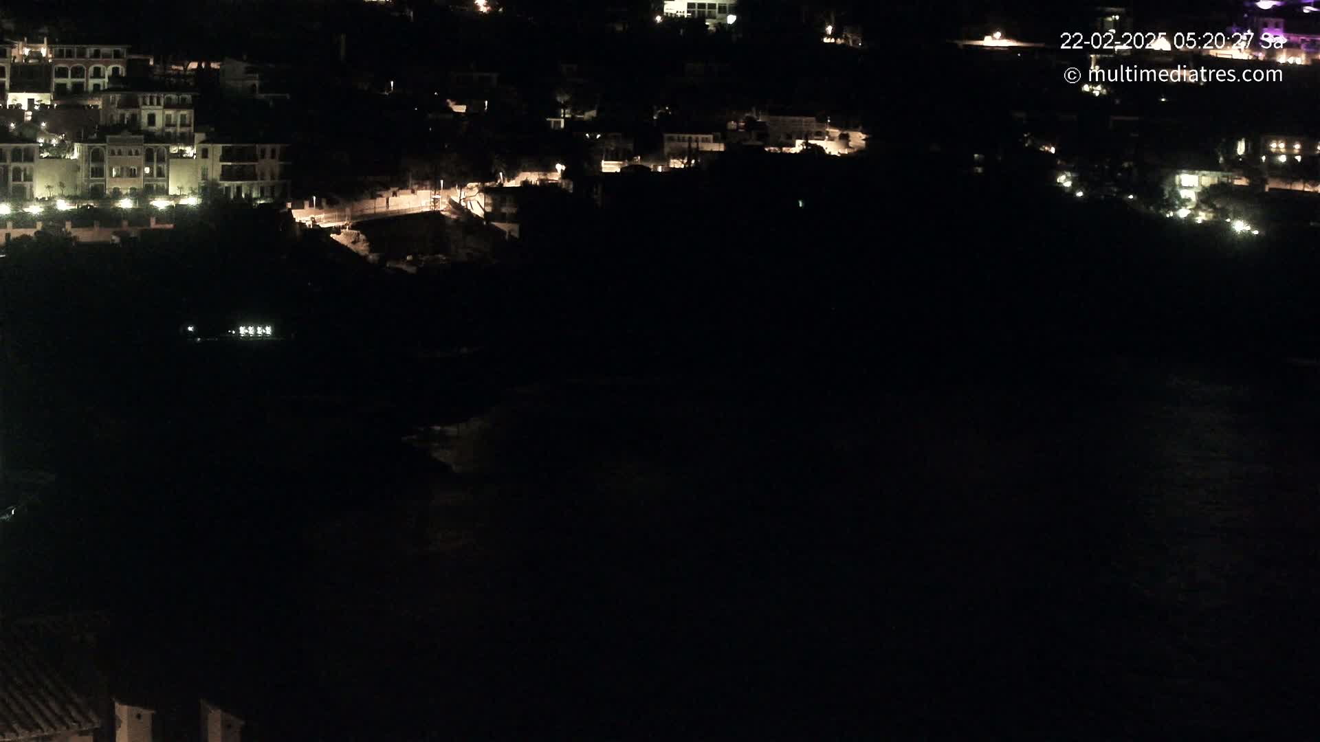 A nighttime view shows a dark body of water below a hillside of illuminated buildings.