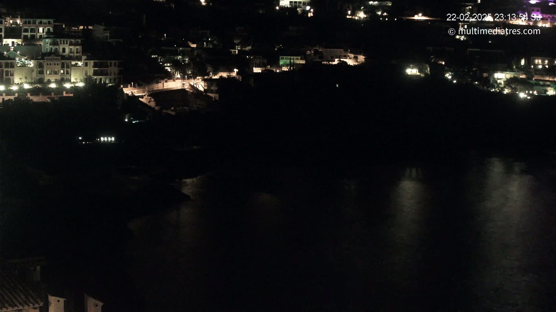 A nighttime view of a coastal town with illuminated buildings overlooking a dark body of water.