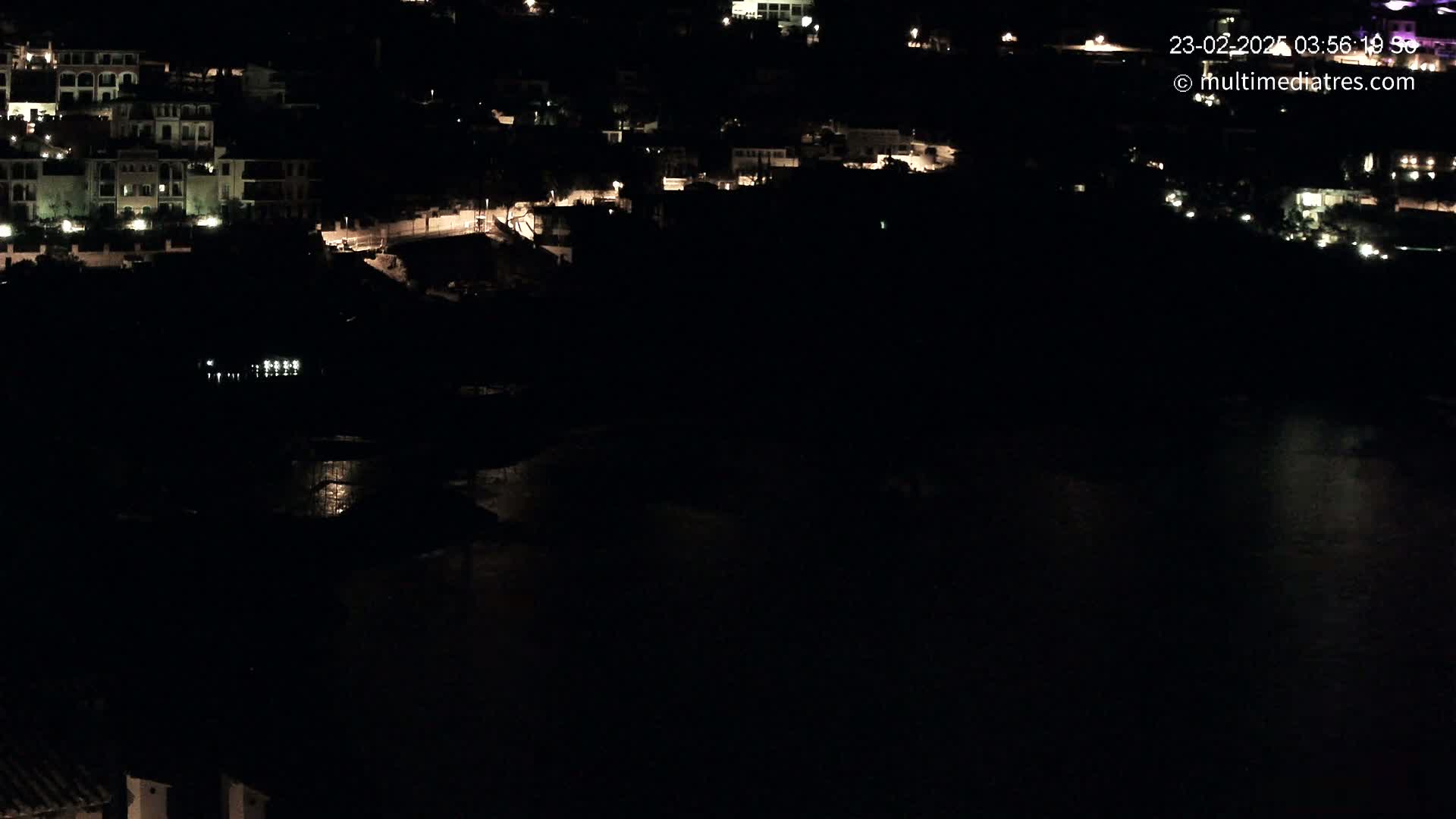 A nighttime, dark view of a coastal town with some lights visible on buildings and the dark water below.