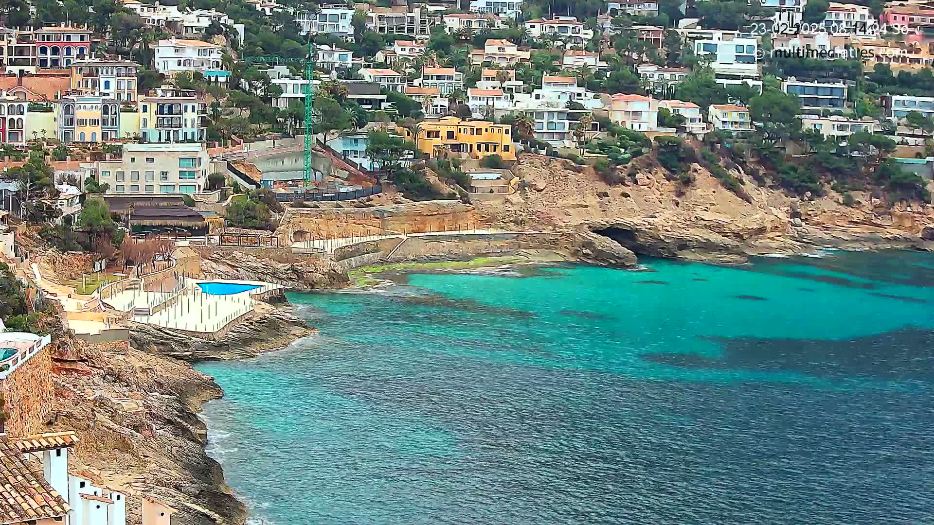 A coastal town with colorful houses built on a rocky hillside overlooking a calm, turquoise sea.