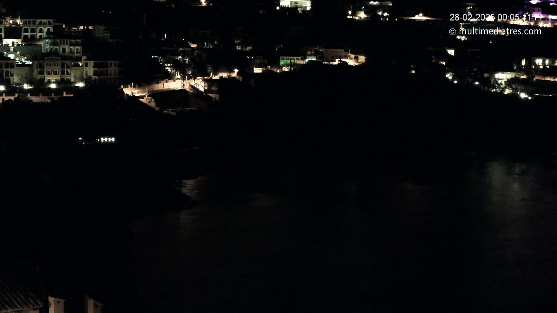A nighttime view of a coastal town with dimly lit buildings and a dark body of water below.