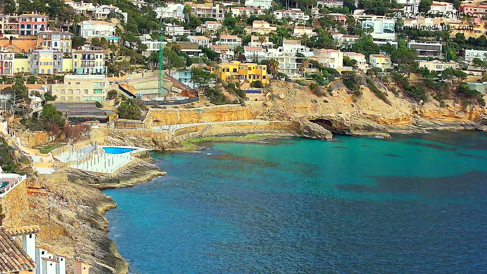 A rocky coastline with colorful houses perched on a hillside overlooking a calm, turquoise sea.