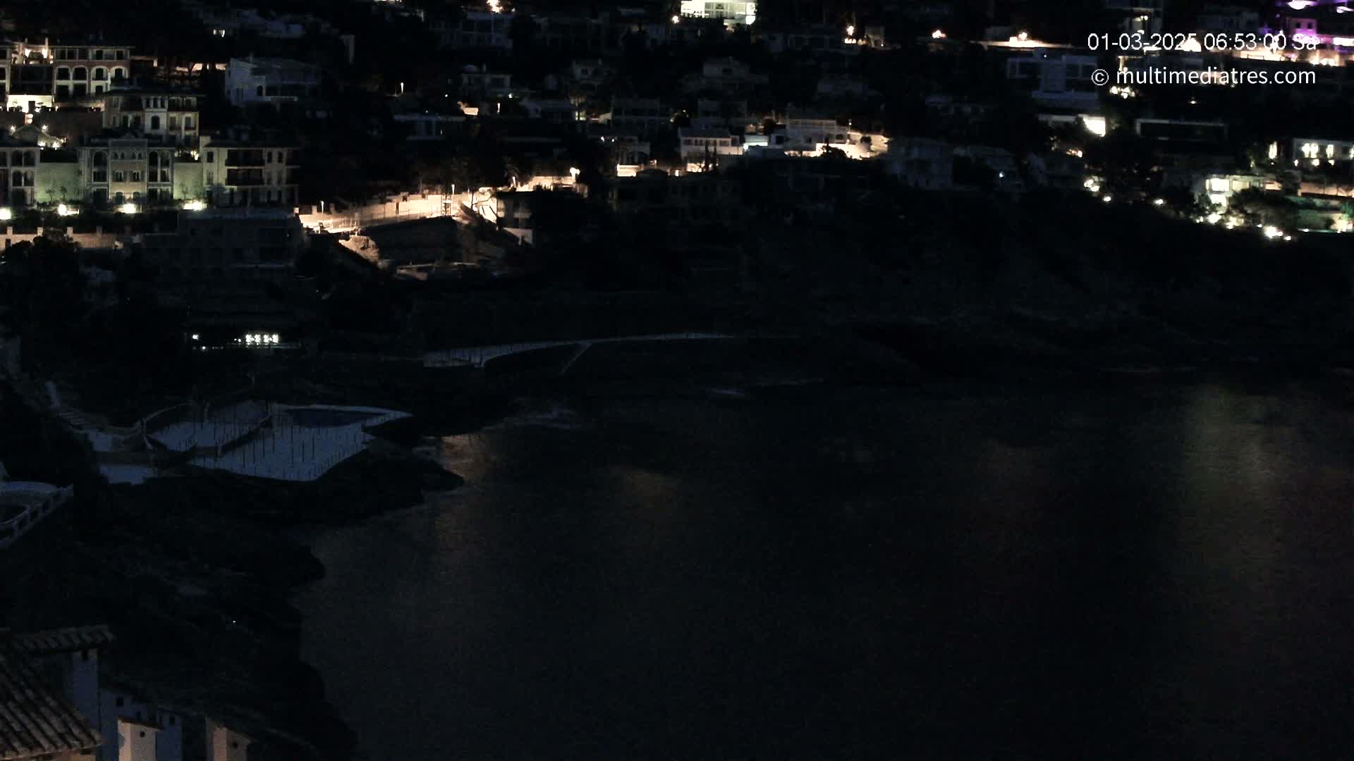 A nighttime view of a coastal town with its lights reflecting on dark water.