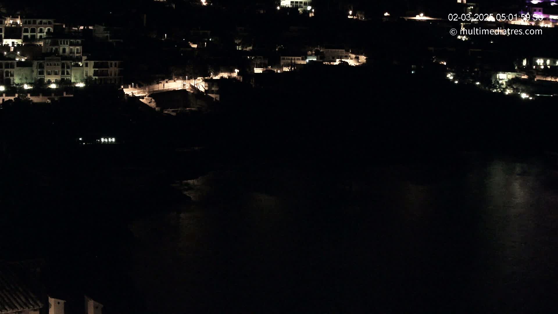 A nighttime view of a coastal town with dimly lit buildings and a dark body of water below.