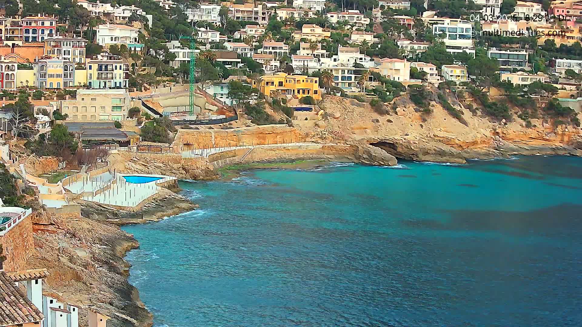 A coastal town with colorful houses built into a rocky hillside overlooking a calm, turquoise sea.
