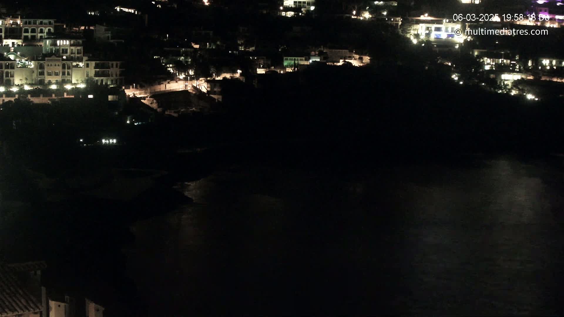 A nighttime view of a coastal town with buildings illuminated against a dark body of water.