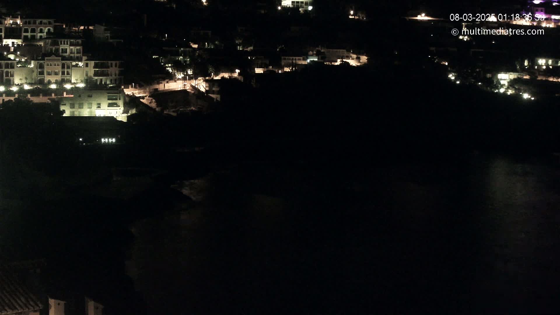 A nighttime view of a coastal town with buildings illuminated, overlooking dark water.