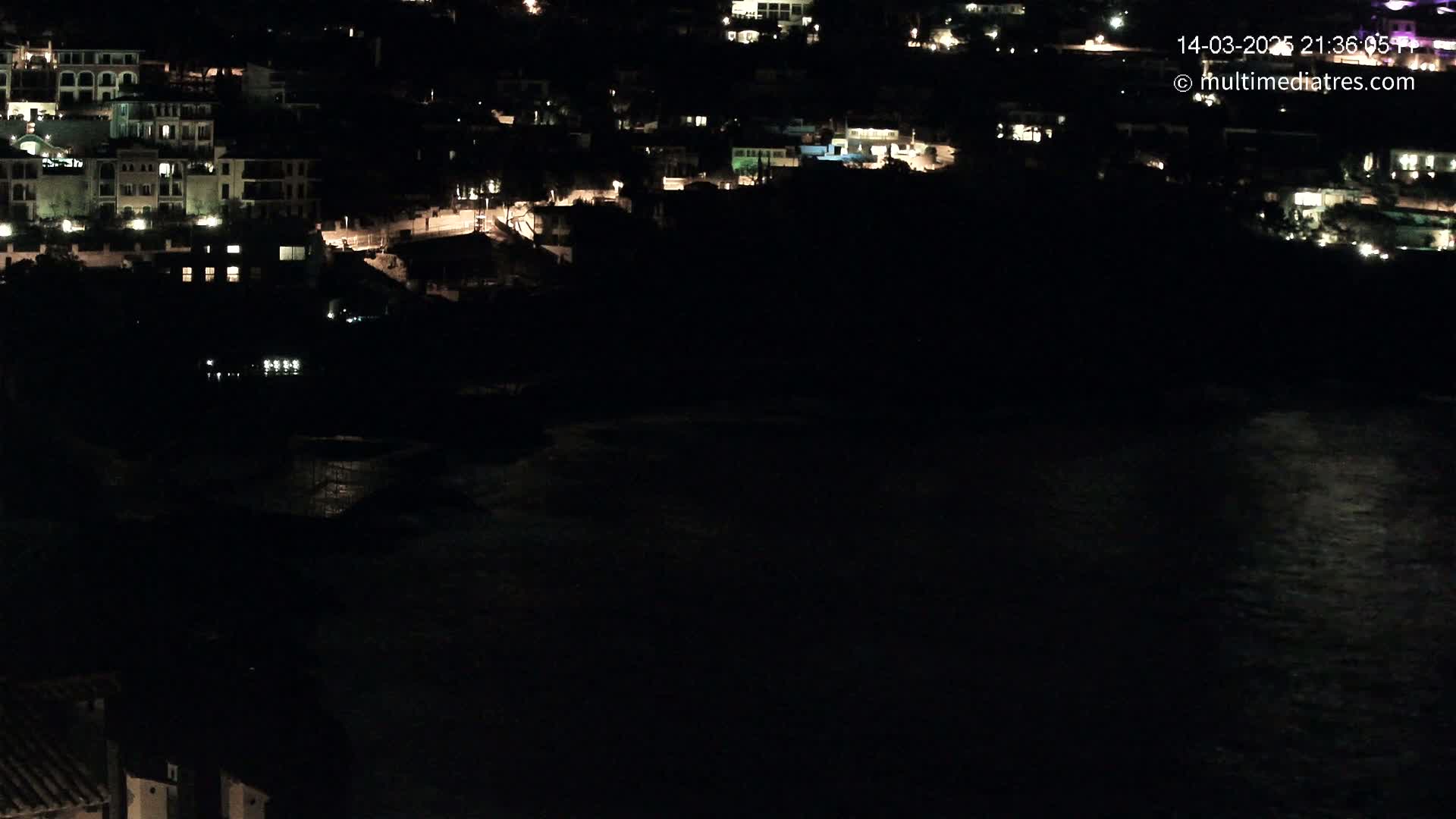 A nighttime view of a coastal town with scattered lights overlooking dark water.