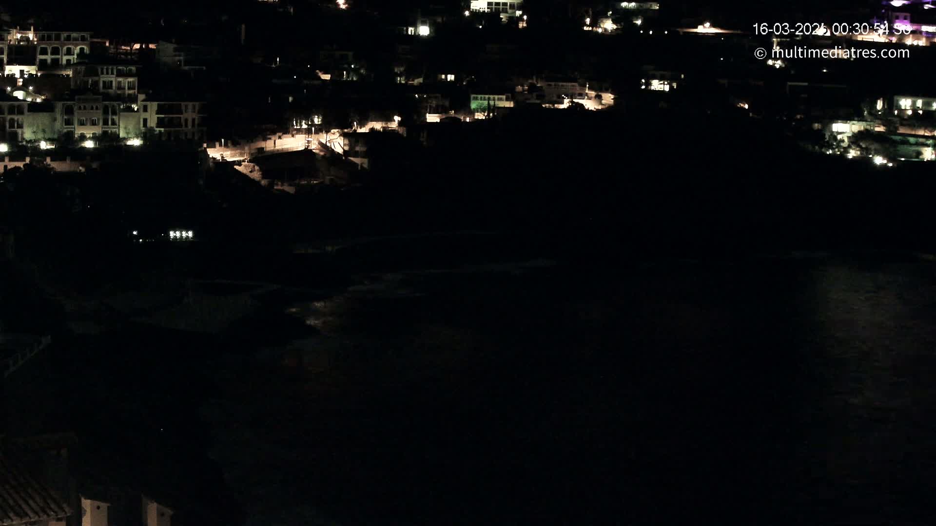 A nighttime view of a coastal town with dimly lit buildings and a dark body of water below.