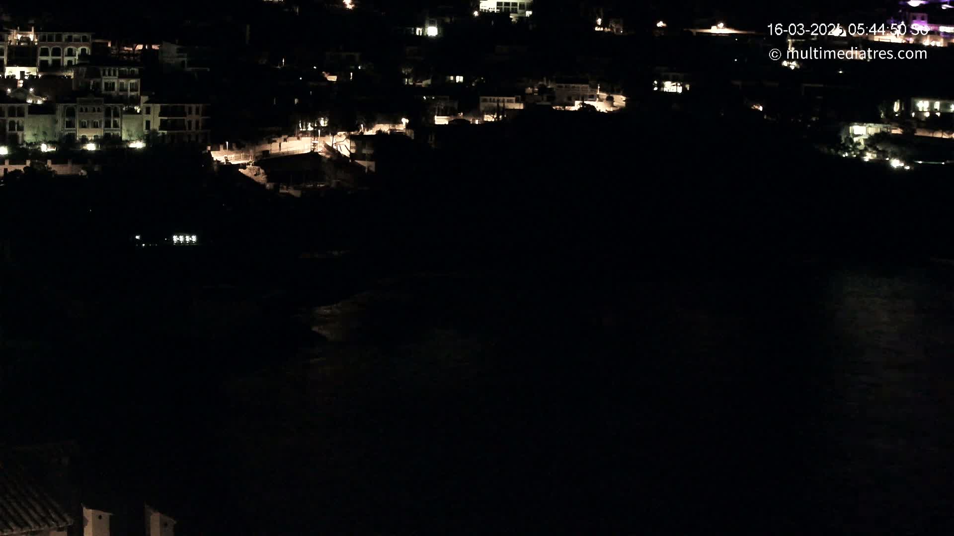 A nighttime view of a coastal town with illuminated buildings and dark water below.