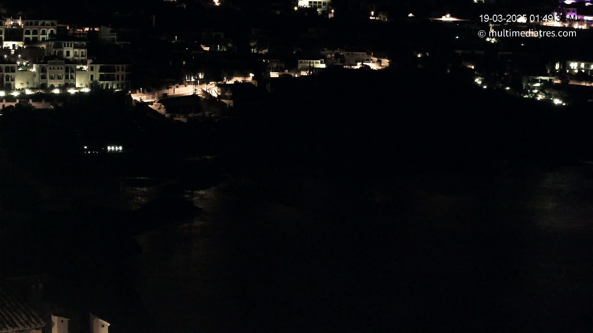 A nighttime view of a coastal town with illuminated buildings overlooking a dark body of water.