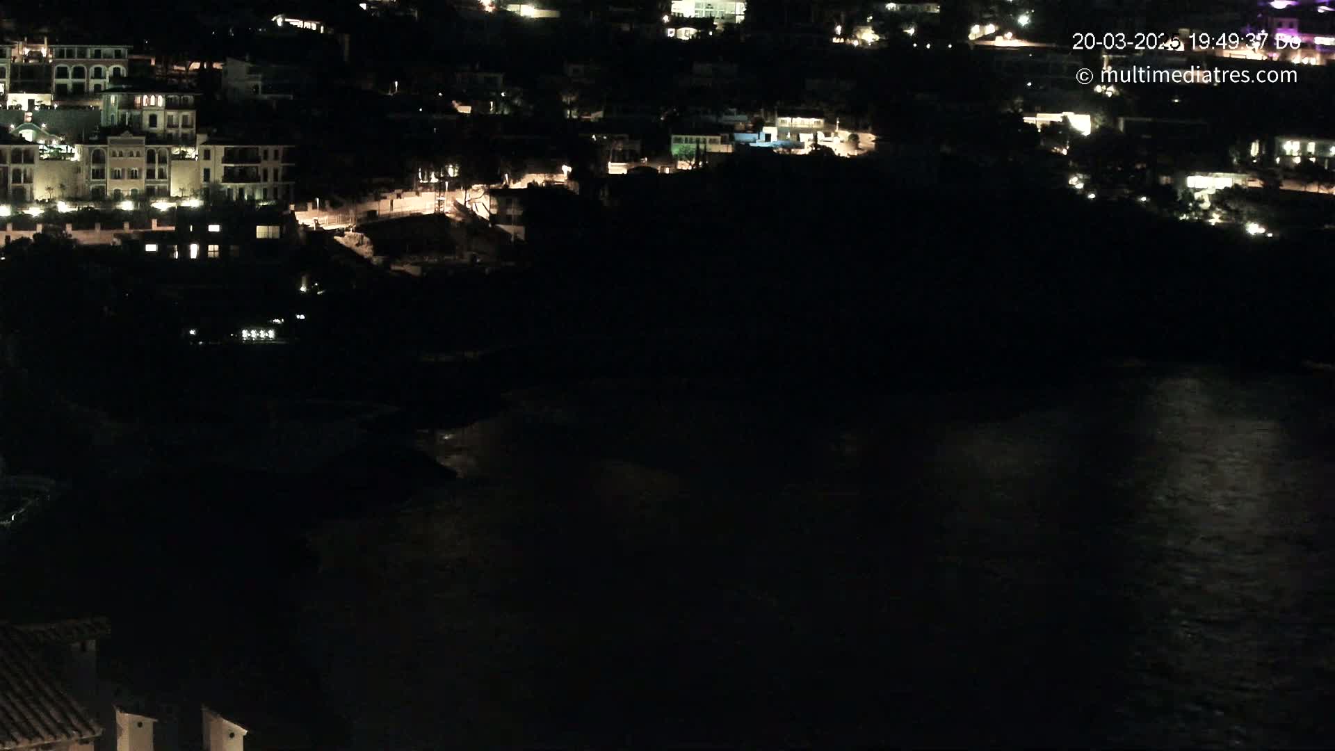 A nighttime view of a coastal town with buildings illuminated against a dark body of water.