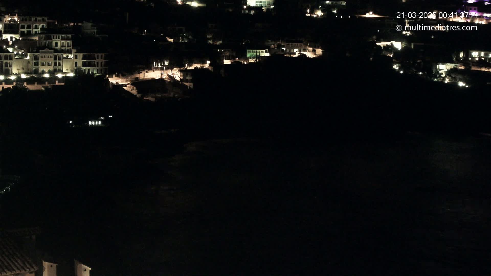 A nighttime view of a coastal town with dimly lit buildings and dark water below.