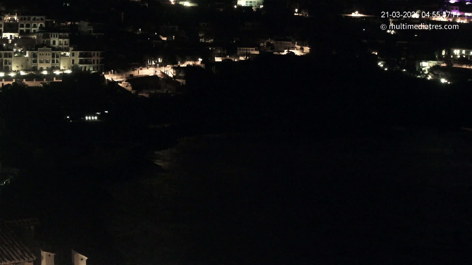 A nighttime view of a coastal town with dimly lit buildings and a dark body of water below.