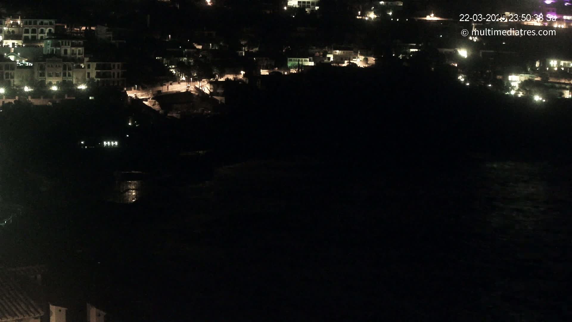 A nighttime, high-angle view of a coastal town with dimly lit buildings and a dark body of water below.