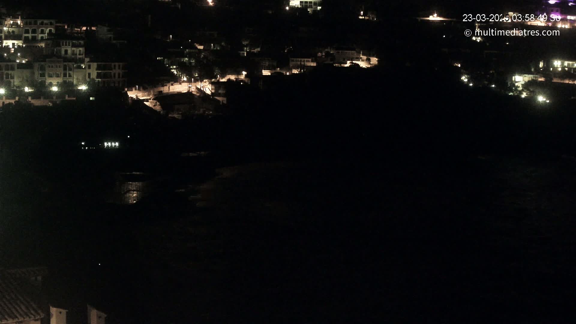 A nighttime view of a coastal town with dimly lit buildings and a dark body of water below.