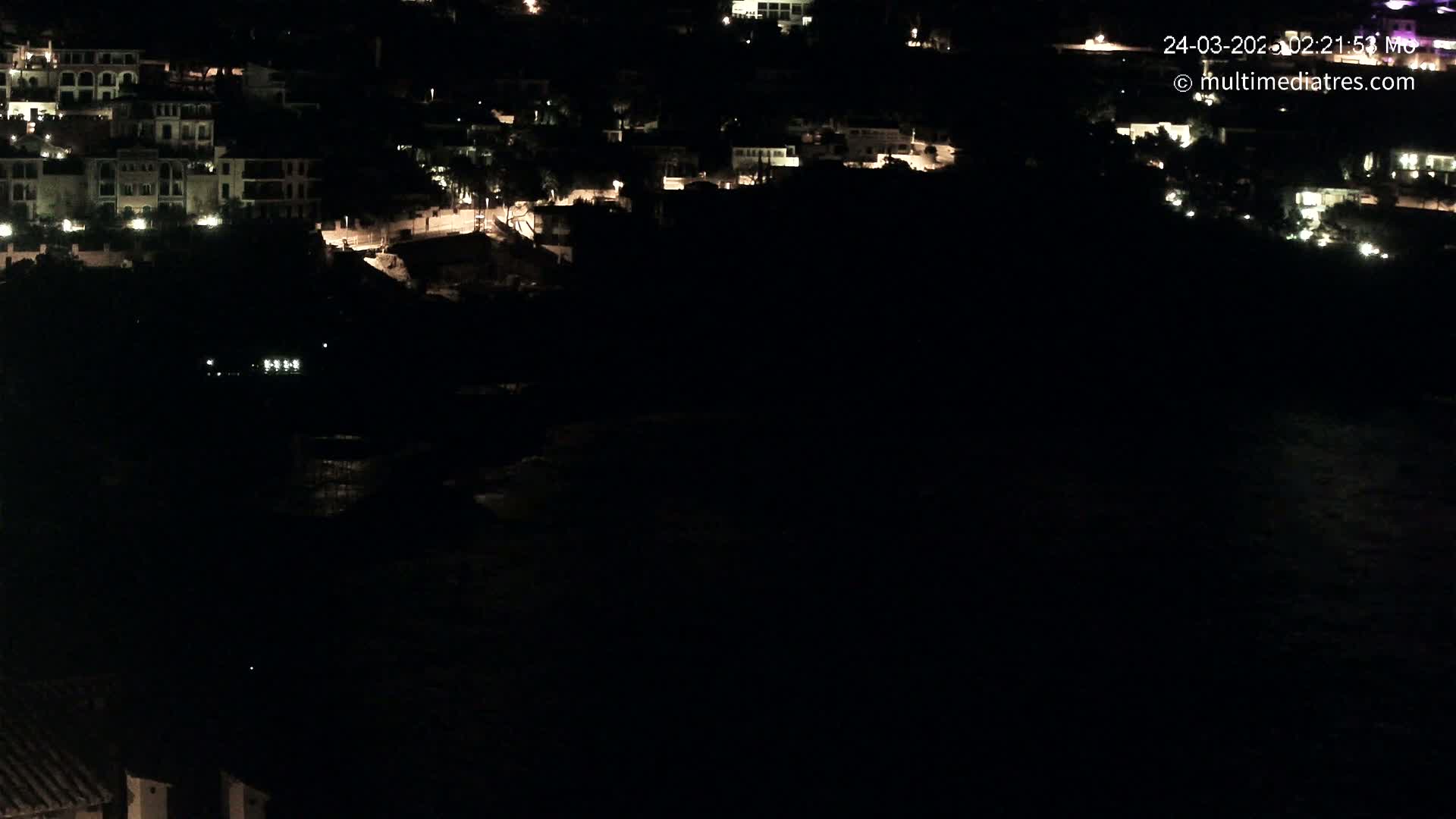 A nighttime, high-angle view shows a cluster of dimly lit buildings along a dark coastline.