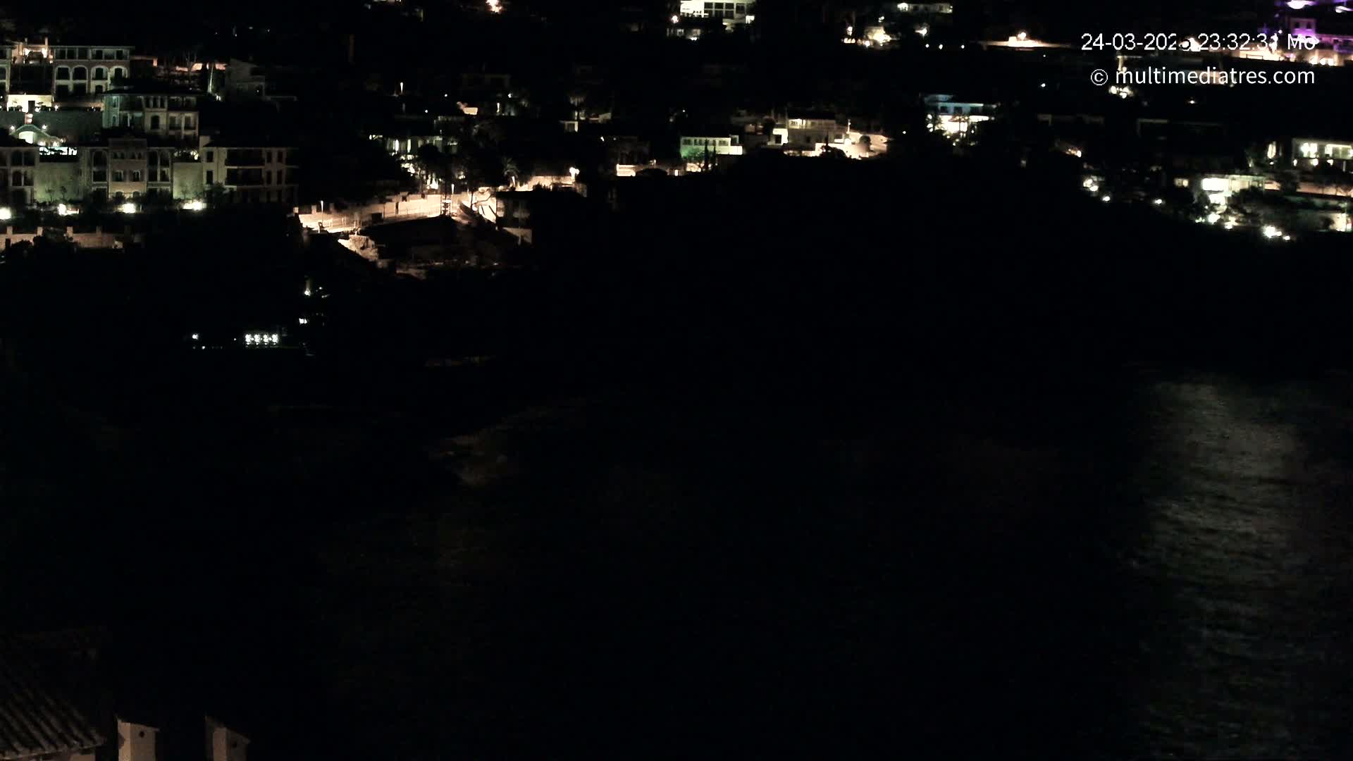 A nighttime view of a coastal town with its lights illuminating buildings and the dark ocean below.