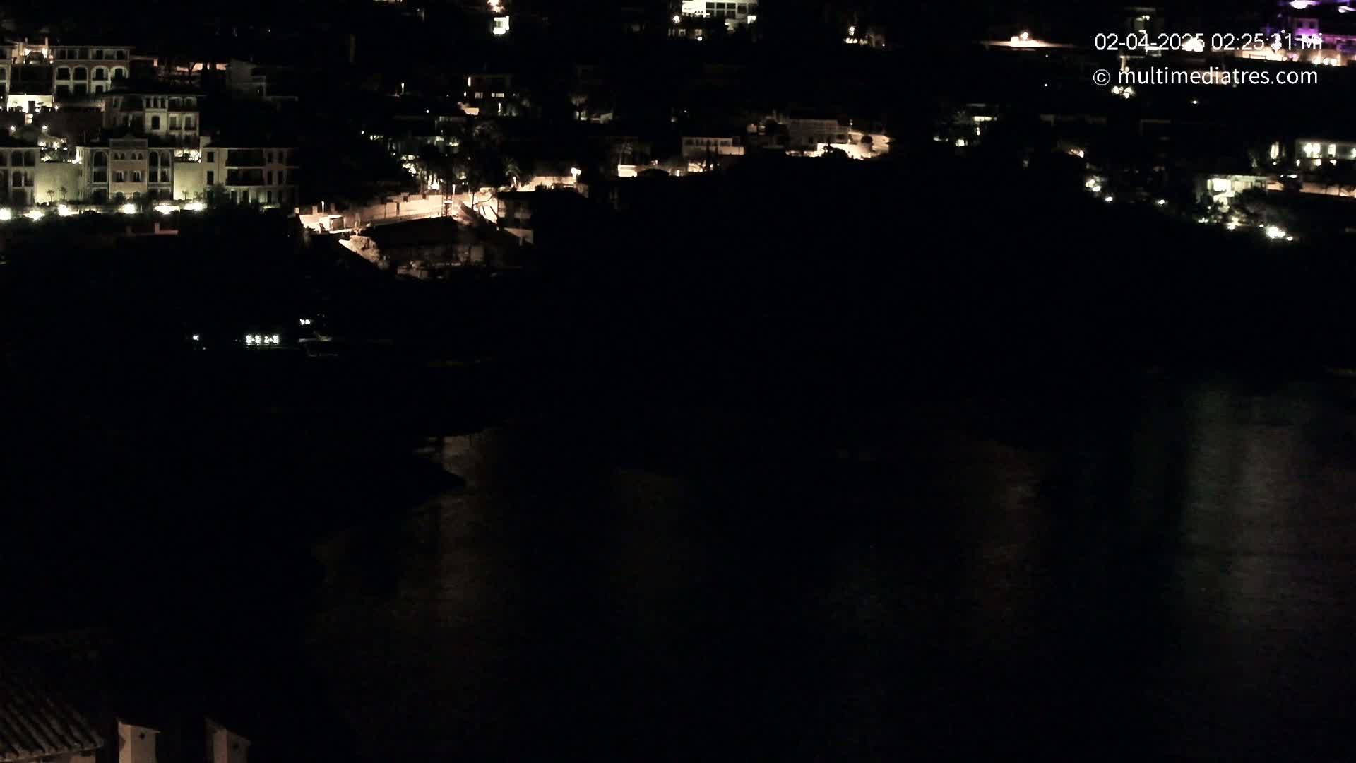 A nighttime view of a coastal town with buildings lit up along a dark body of water.