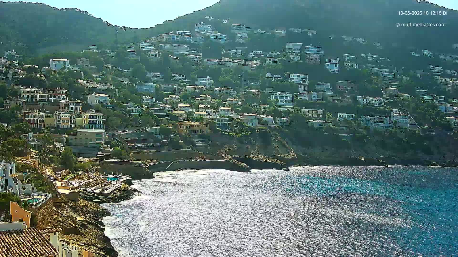 A hillside densely populated with houses overlooks a sparkling blue ocean on a sunny day.