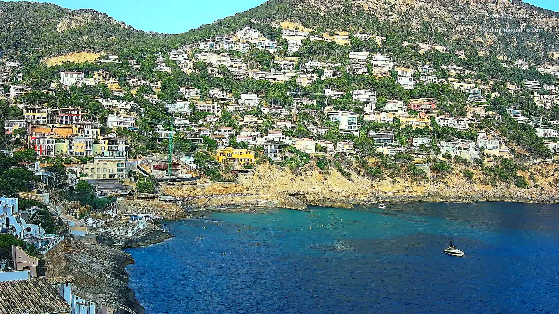 A hillside town of colorful houses cascading down to a calm, blue ocean cove on a clear, sunny day.