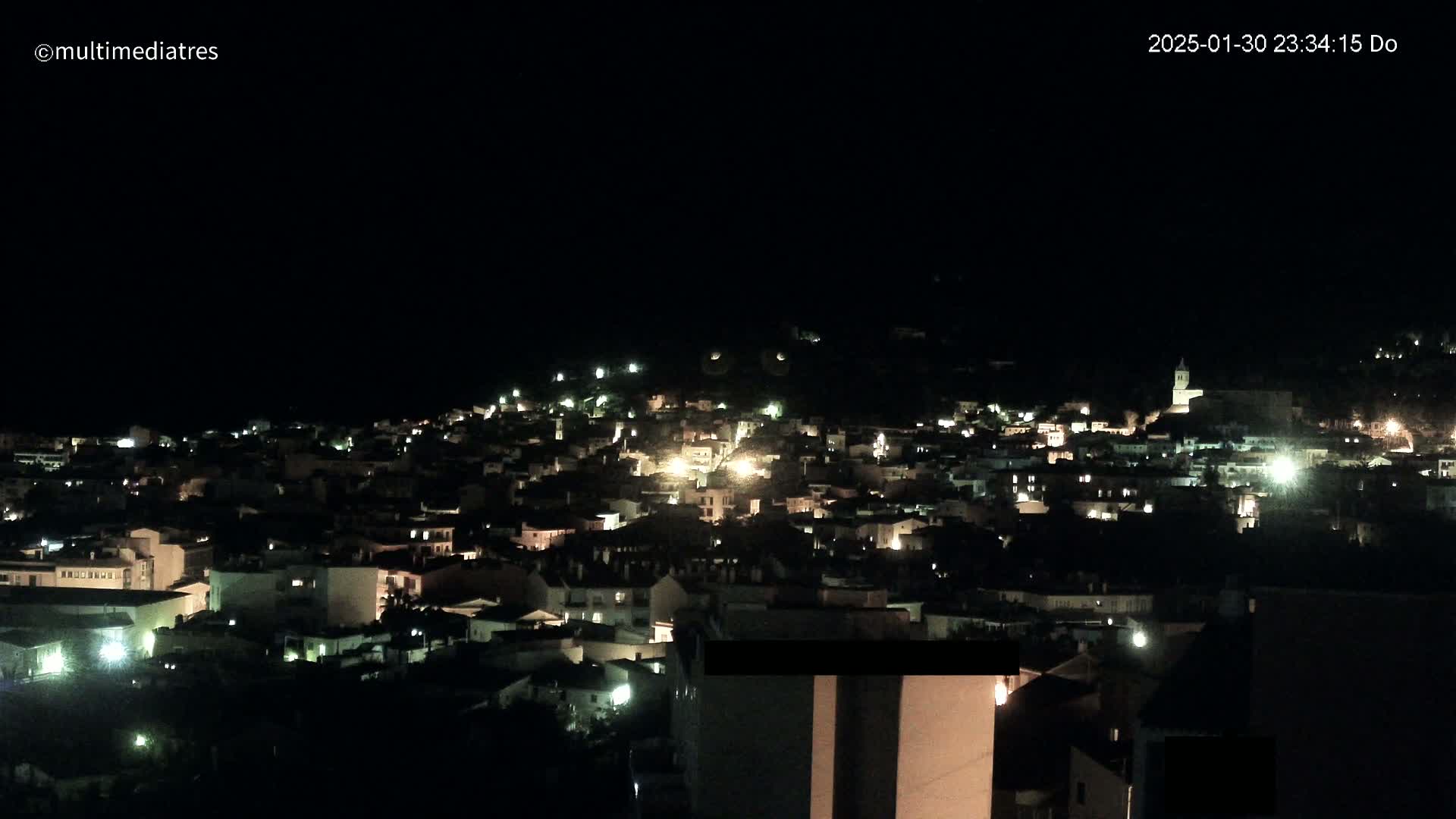 A nighttime, high-angle view of a town illuminated by scattered lights.