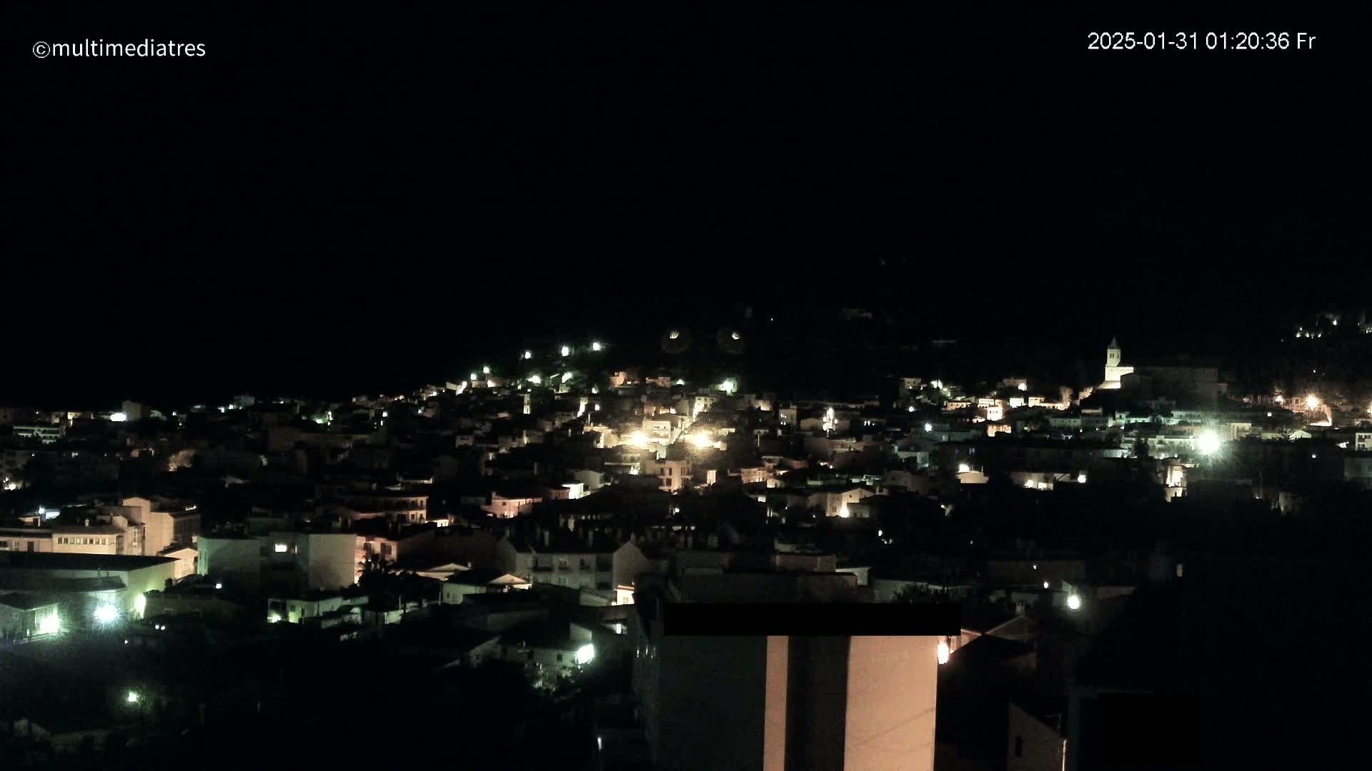 A nighttime, high-angle view of a town illuminated by scattered lights.