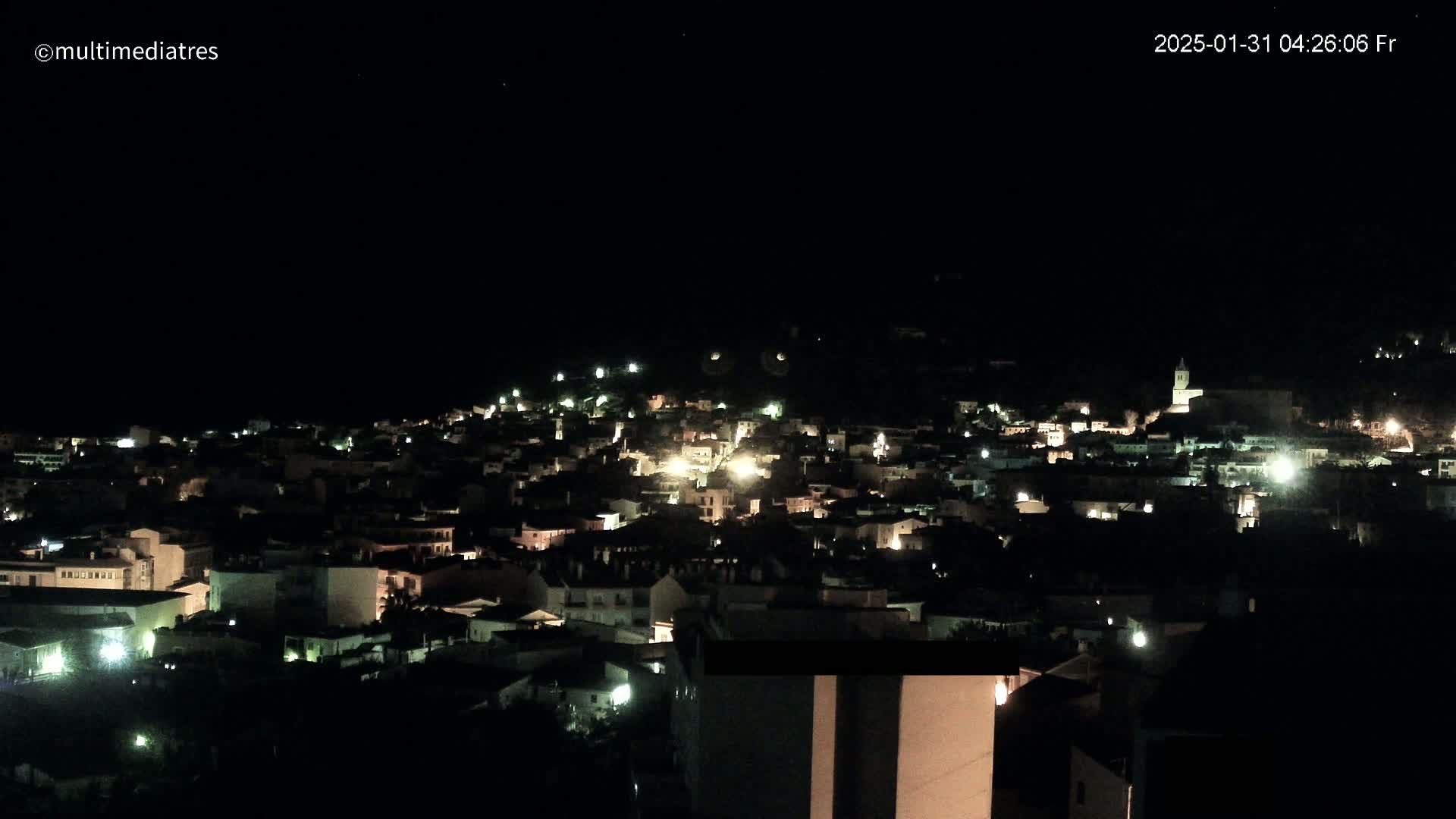 A small town at night, illuminated by scattered lights, under a clear, dark sky.