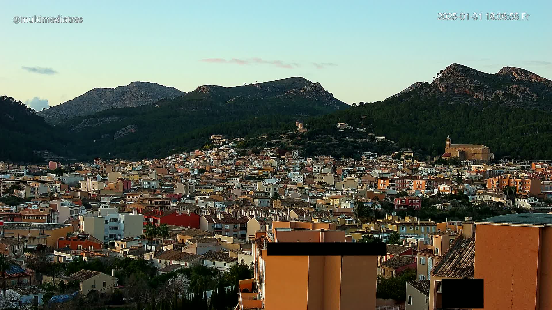 A dense collection of low-rise buildings situated at the base of a large, mountainous region under a clear, twilight sky.