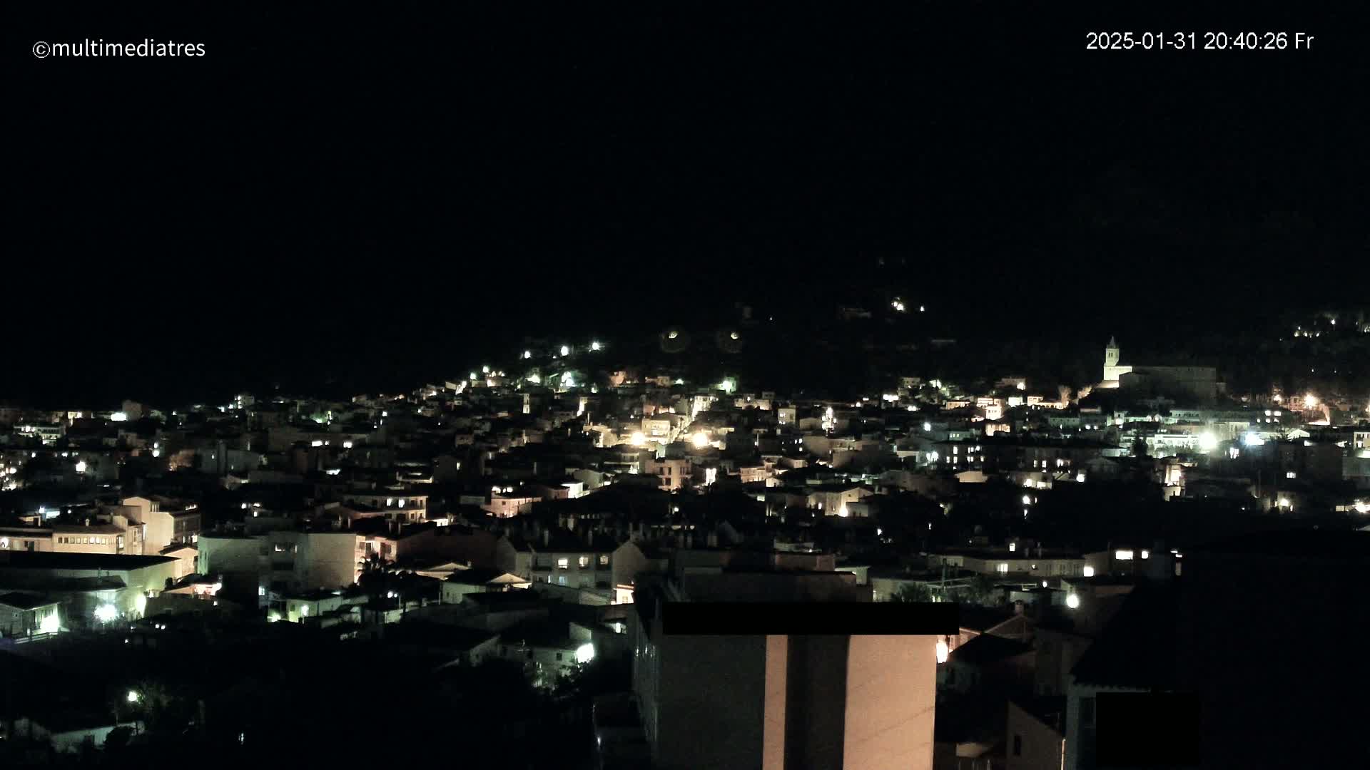 A nighttime, aerial view shows a town illuminated by scattered lights against a completely dark sky.