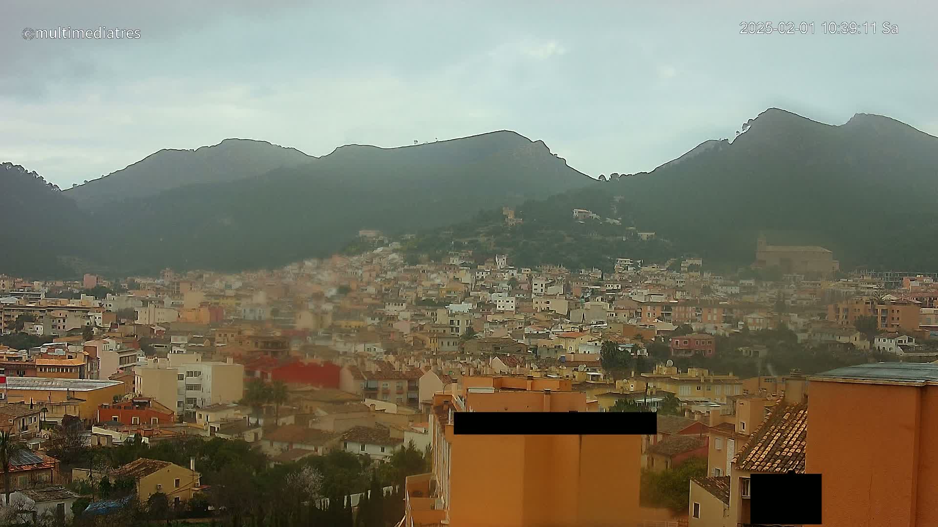 A sprawling town nestled at the base of a mountain range under an overcast sky.