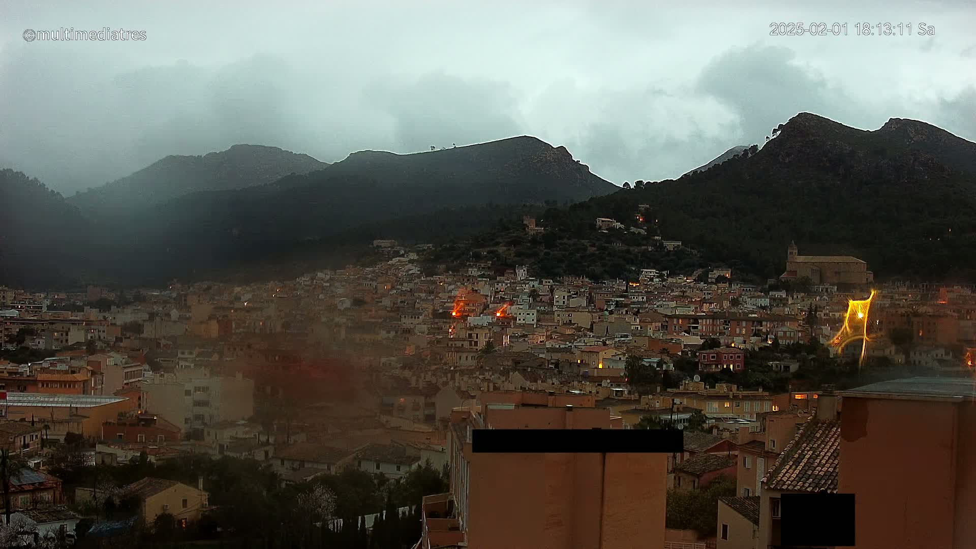 A town nestled in a valley between dark, hazy mountains under an overcast sky.