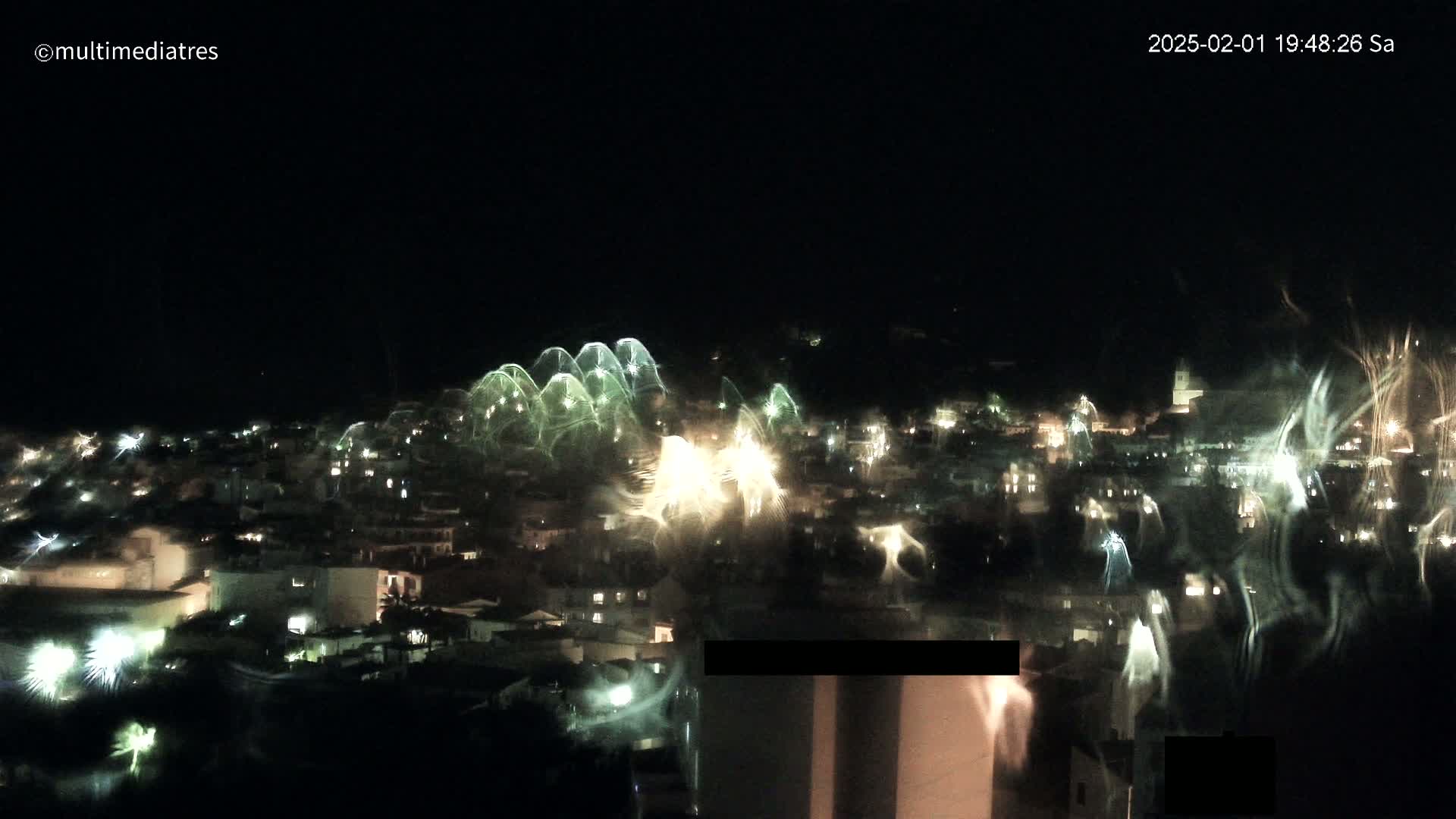 A nighttime view of a town with fireworks exploding over it.