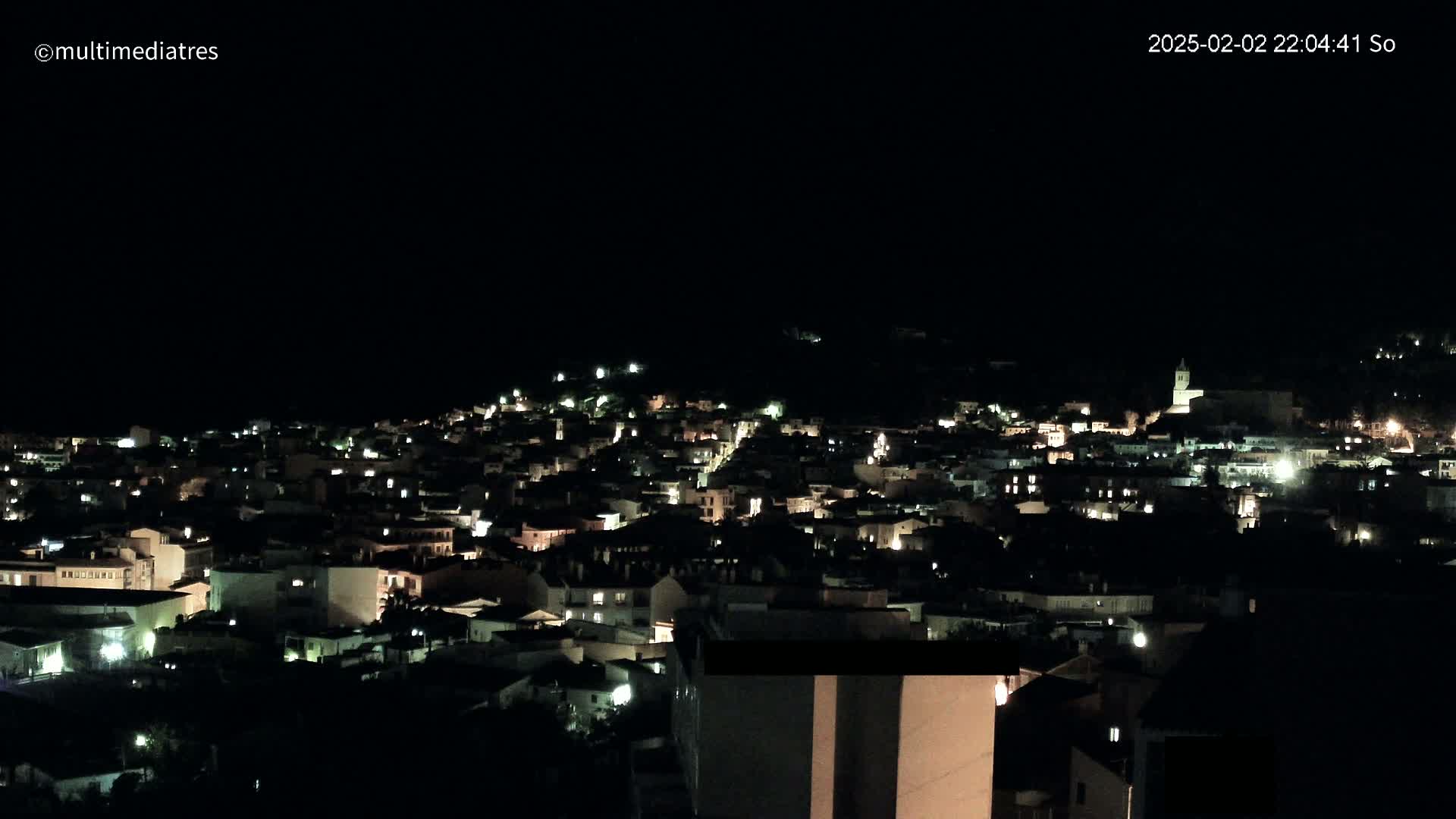 A hillside town is illuminated at night under a clear, dark sky.