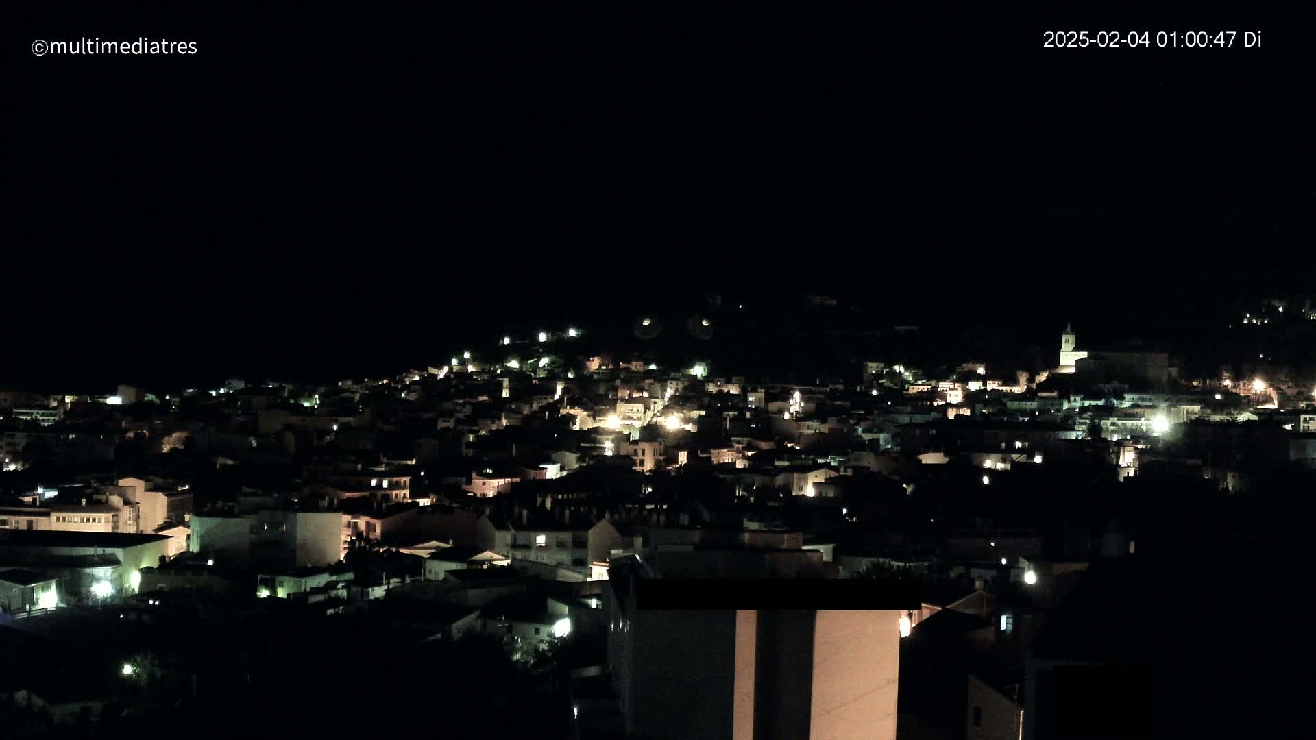 A nighttime, aerial view shows a town illuminated by scattered lights against a completely dark sky.