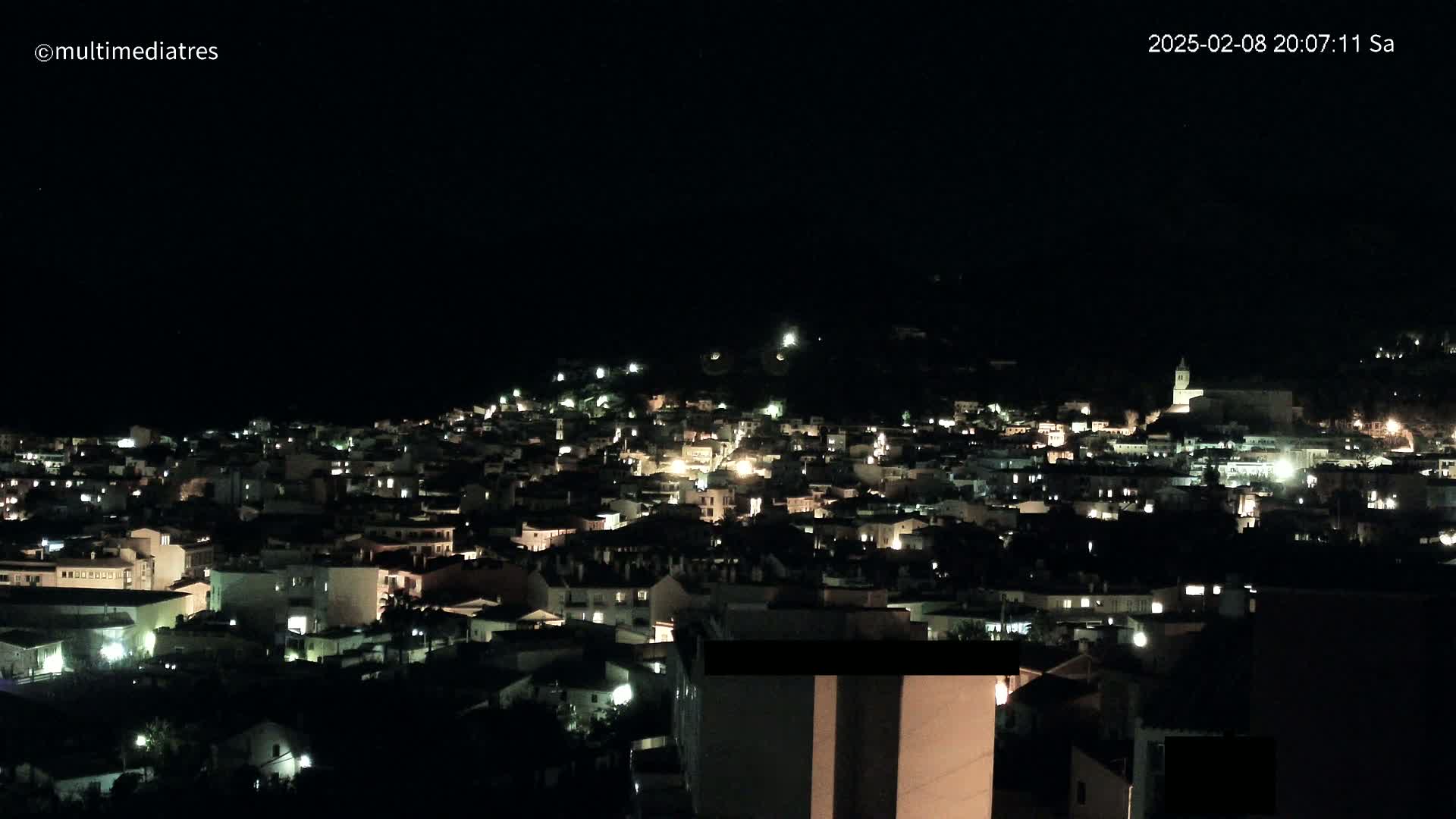 A hillside town is illuminated at night under a clear, dark sky.