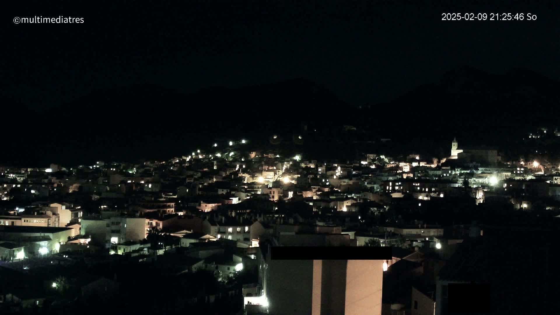 A nighttime view of a town nestled on a hillside, illuminated by scattered lights.