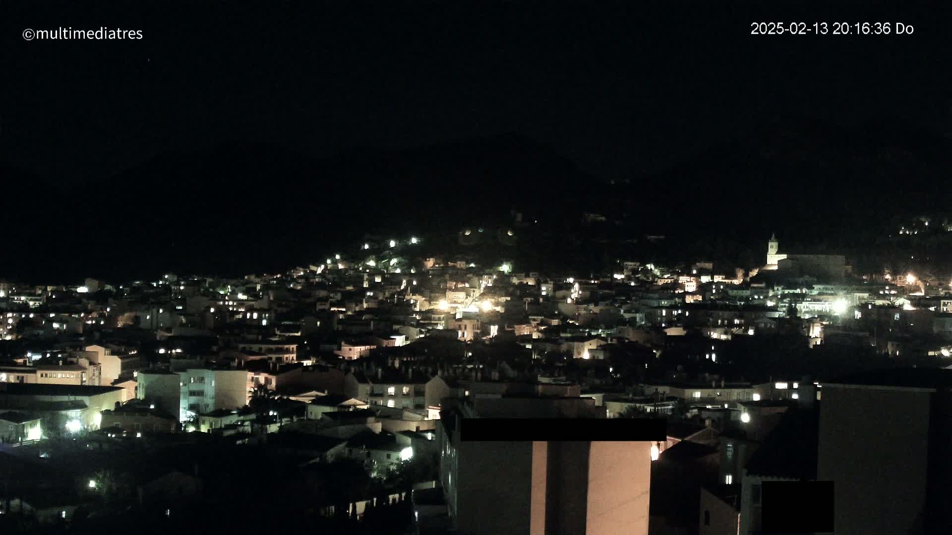 A nighttime view of a town nestled on a hillside, illuminated by scattered lights.
