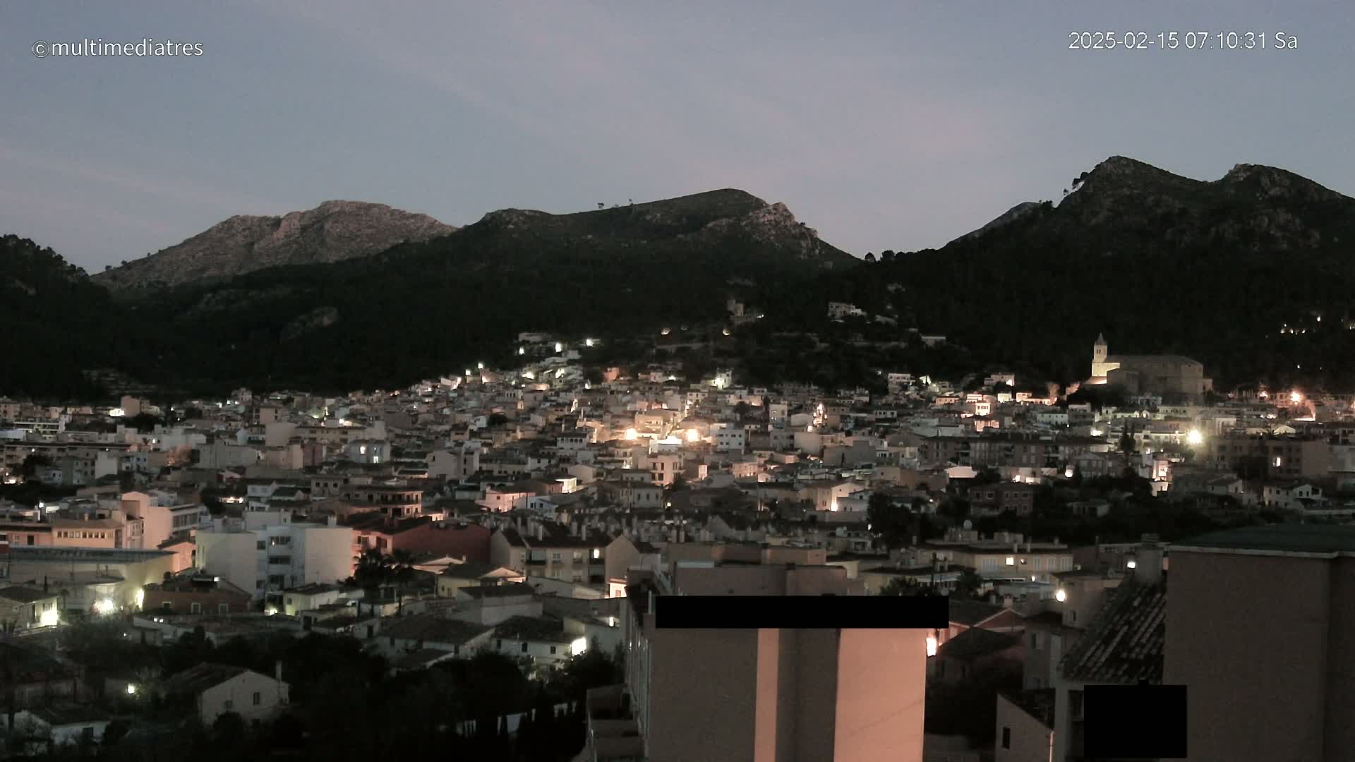A town nestled in a valley between dark, mountainous terrain at twilight.