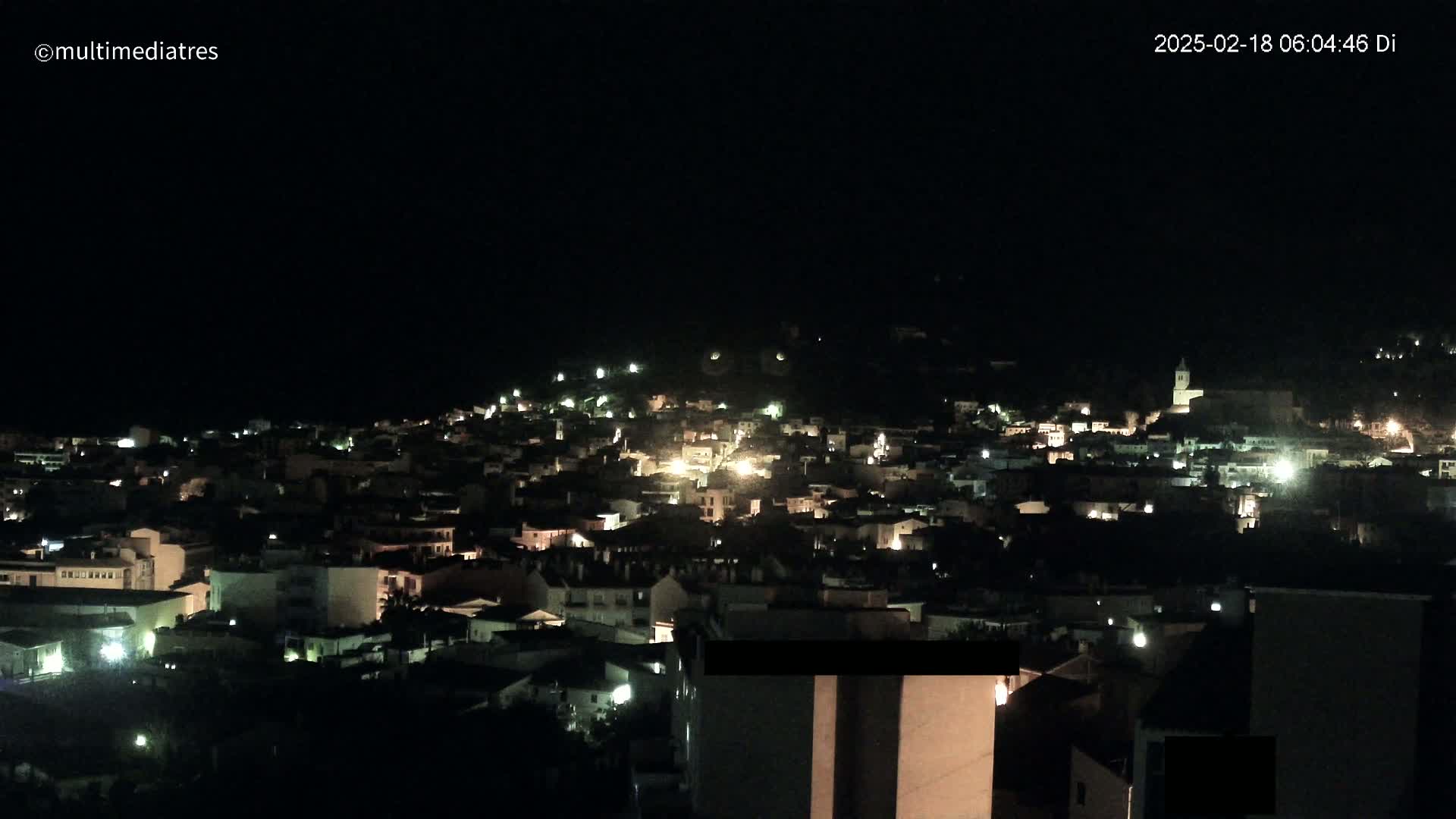 A nighttime, aerial view of a town with many buildings lit up, under a dark, clear sky.