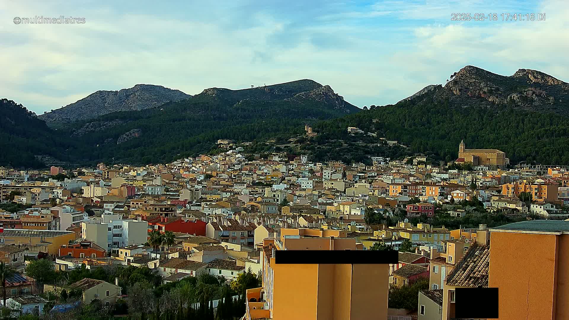 A sprawling town of colorful buildings nestles at the base of a mountain range under a mostly clear sky.