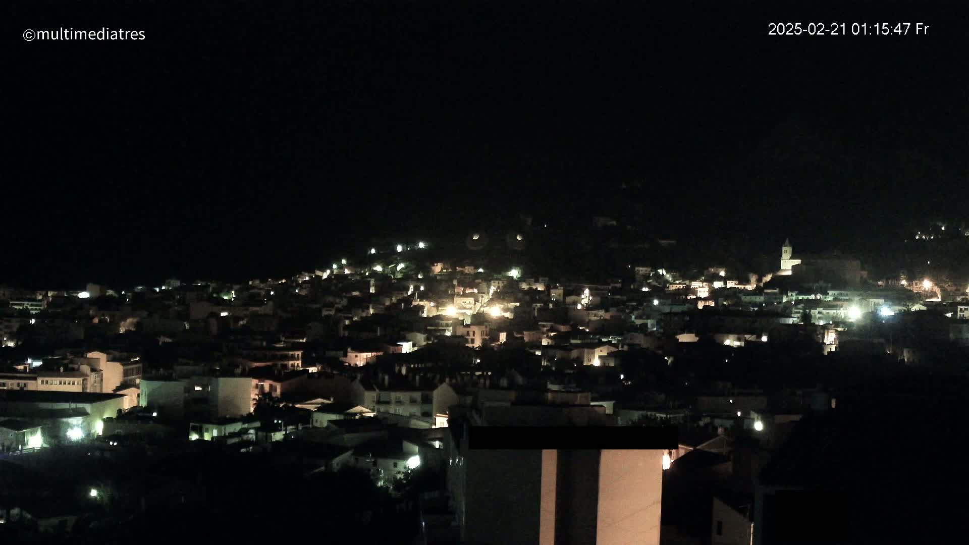 A nighttime, aerial view shows a town's buildings illuminated by scattered interior lights.