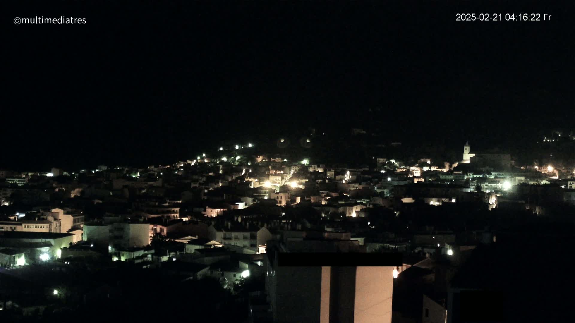 A nighttime, high-angle view of a town illuminated by scattered lights.