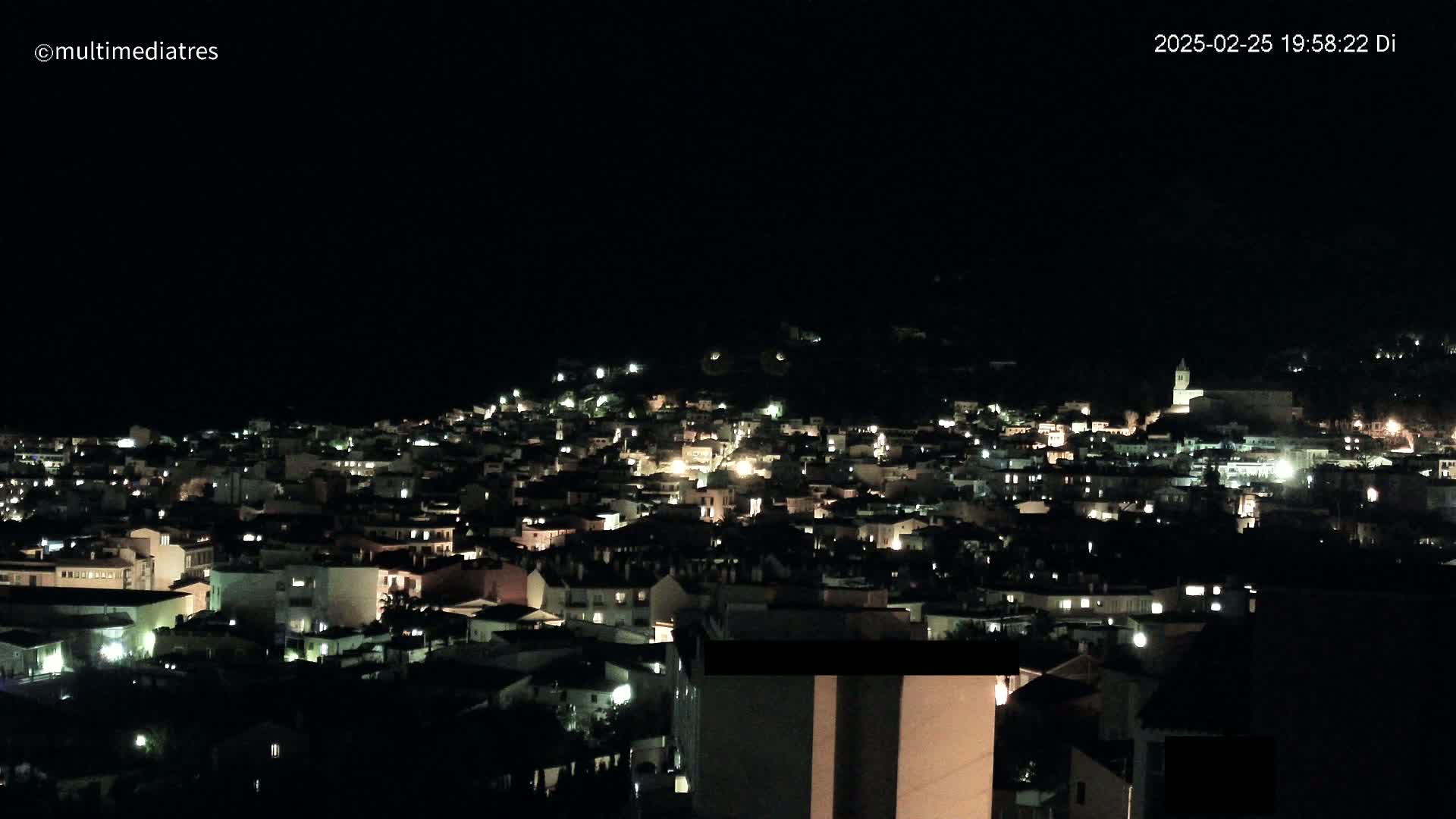 A hillside town is illuminated at night under a clear, dark sky.