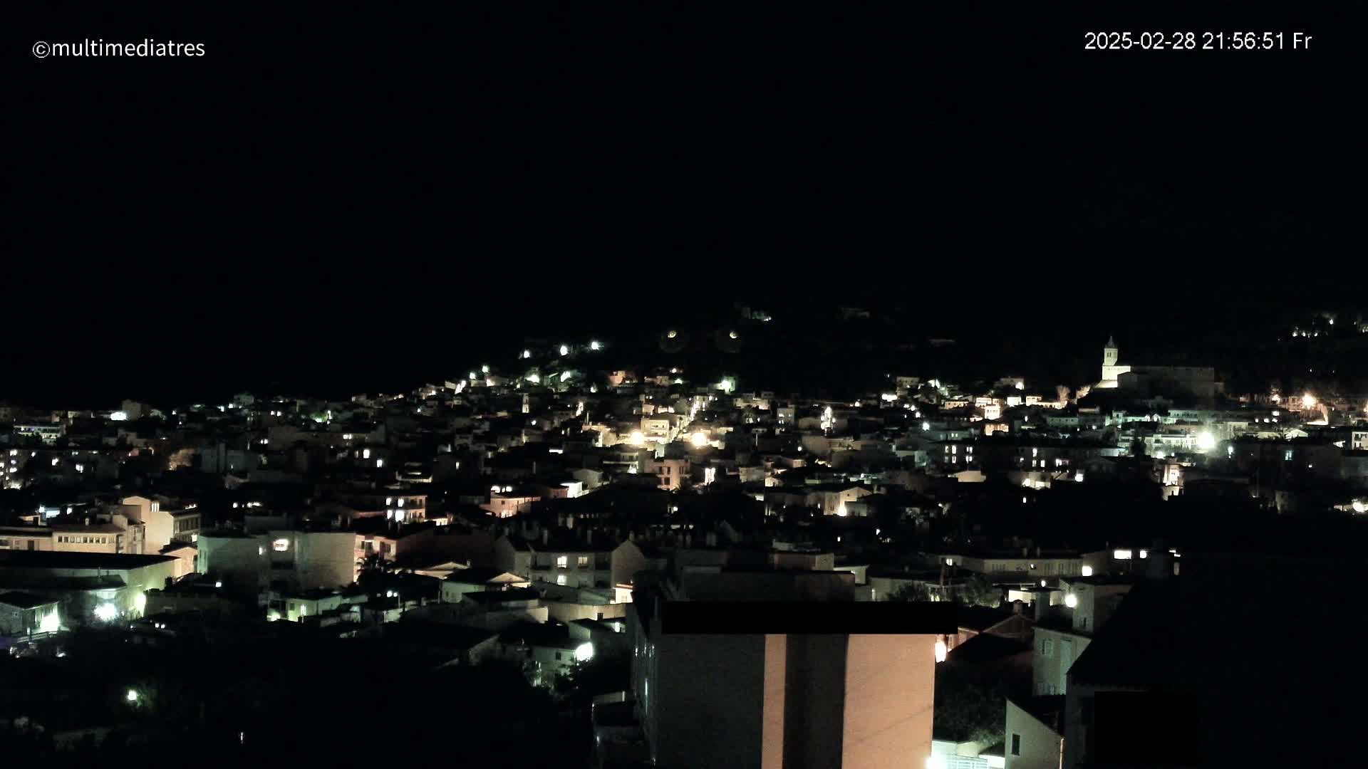 A nighttime view of a town nestled on a hill, illuminated by scattered lights.